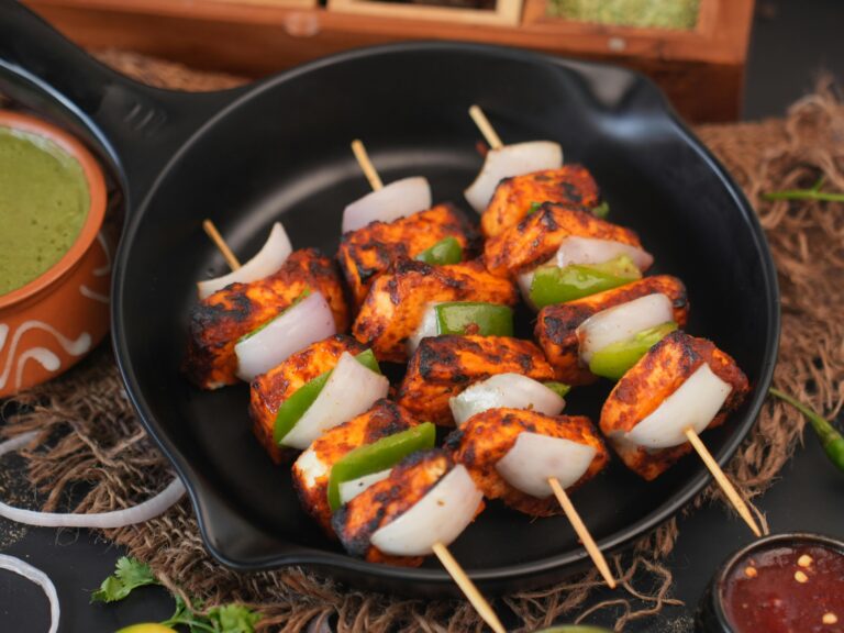 Close-up of grilled paneer skewers with bell peppers and onions on black plate.